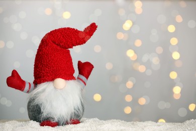 Photo of Cute Christmas gnome on snow against blurred festive lights. Space for text