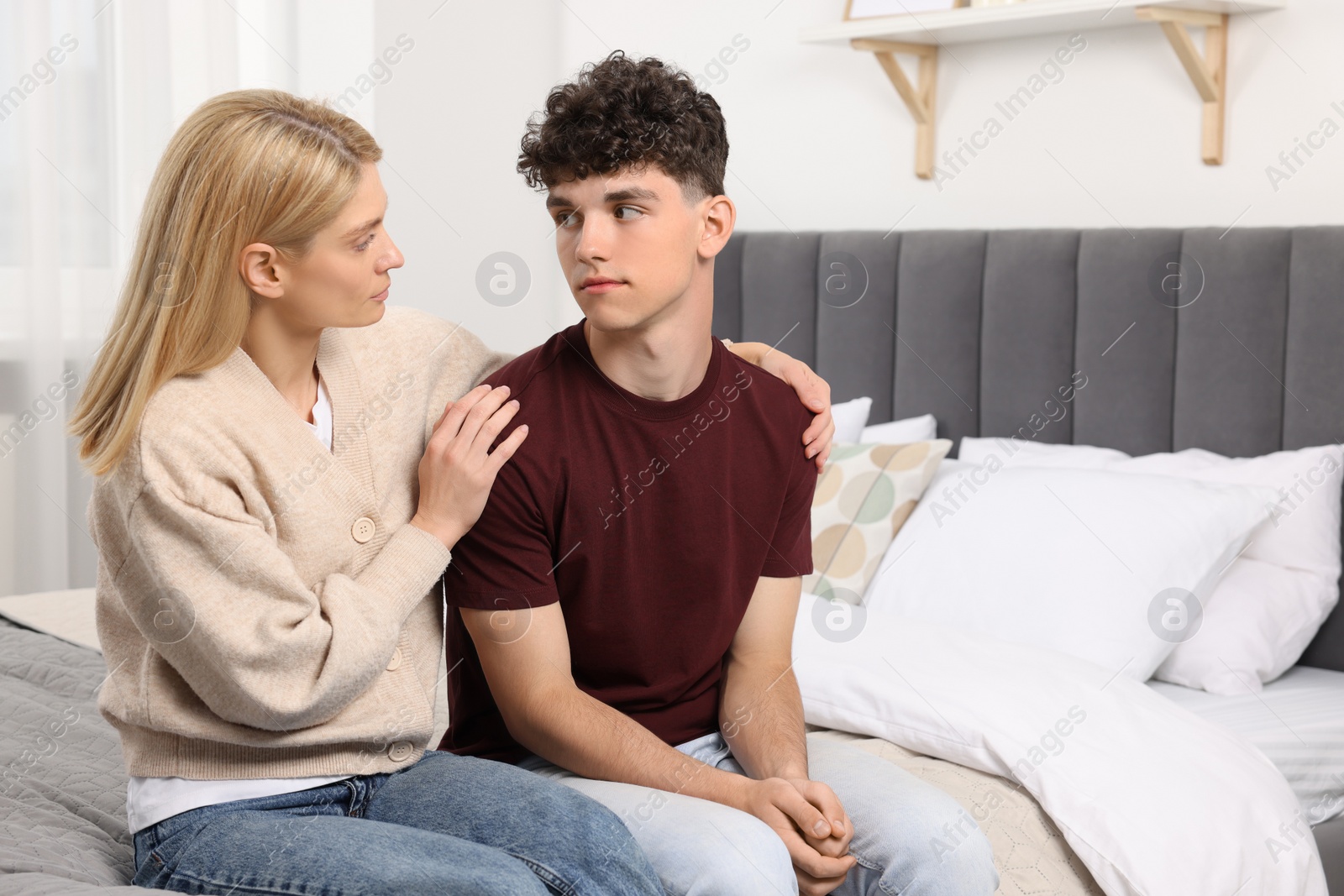 Photo of Mother consoling her upset son in bedroom, space for text. Teenager problems