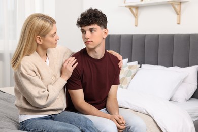 Photo of Mother consoling her upset son in bedroom, space for text. Teenager problems