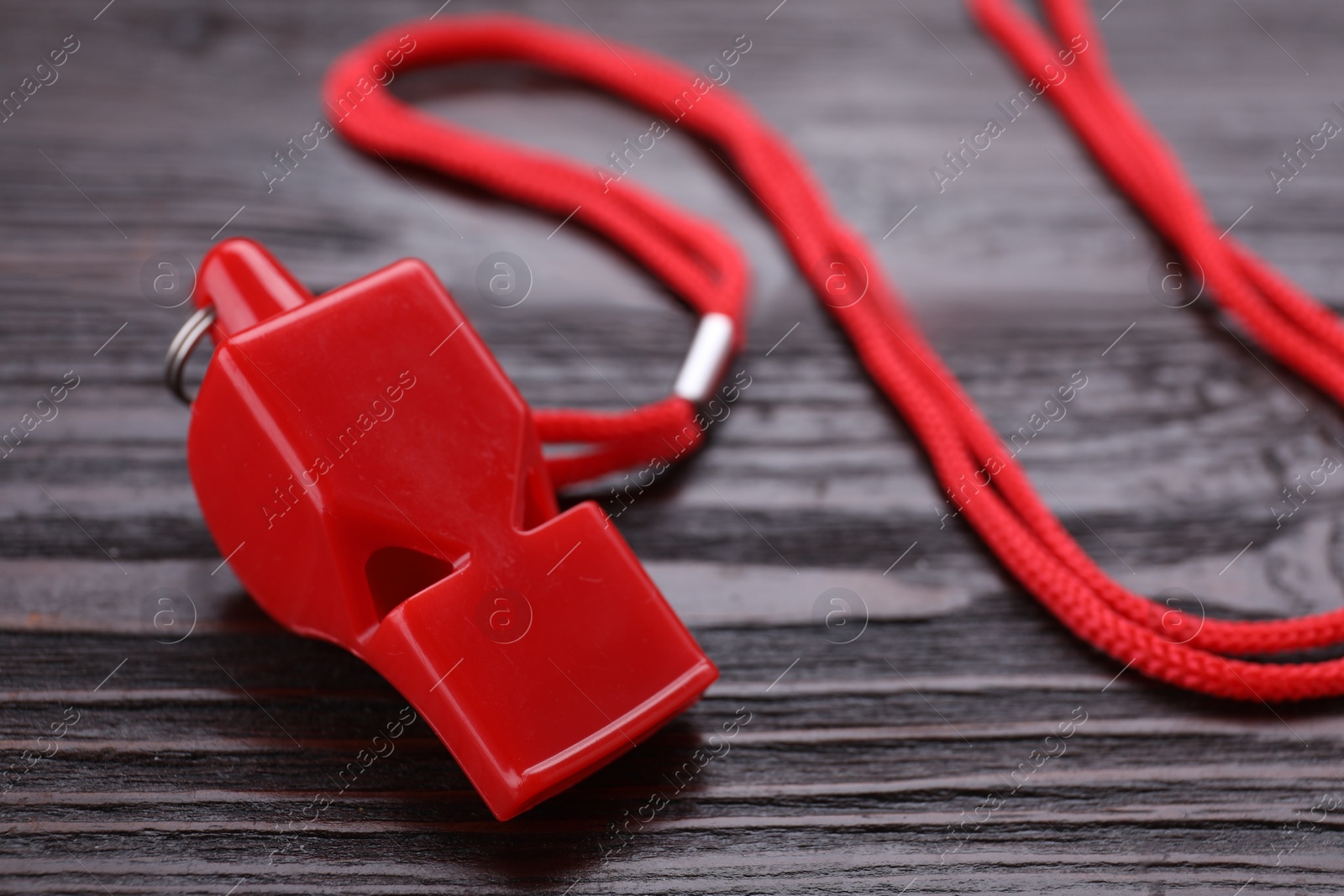 Photo of One red whistle with cord on wooden table, closeup