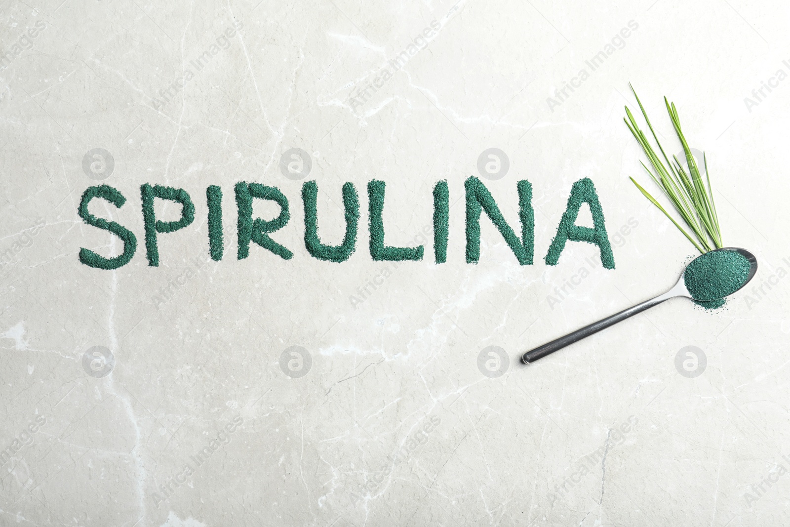 Photo of Word SPIRULINA made of algae powder, spoon and grass on light background, top view