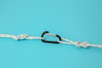 Photo of One metal carabiner with ropes on light blue background