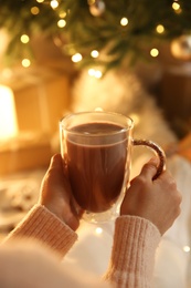 Woman with cup of drink and blurred Christmas lights on background, closeup