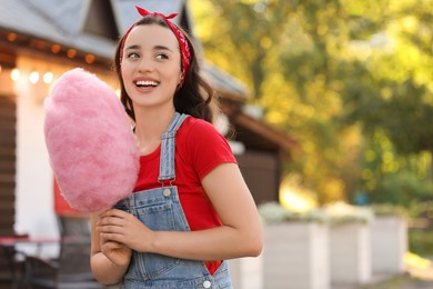 Photo of Stylish young woman with cotton candy outdoors, space for text