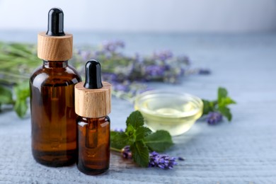 Photo of Bottles of essential oil, mint and fresh lavender on grey wooden table, space for text