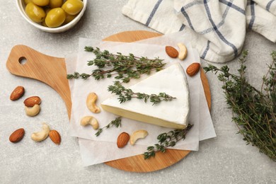 Photo of Piece of tasty camembert cheese, thyme, nuts and olives on grey textured table, flat lay