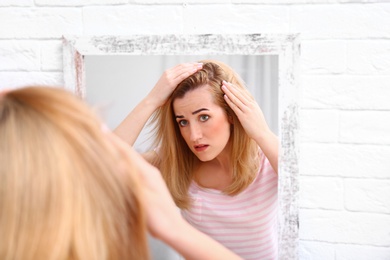 Photo of Young woman with hair loss problem near mirror indoors