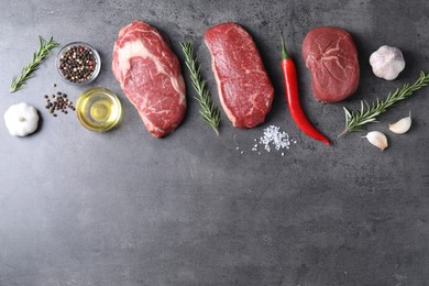 Photo of Raw beef steaks, oil and spices on grey table, flat lay. Space for text