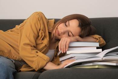 Photo of Young tired woman sleeping near books on couch indoors