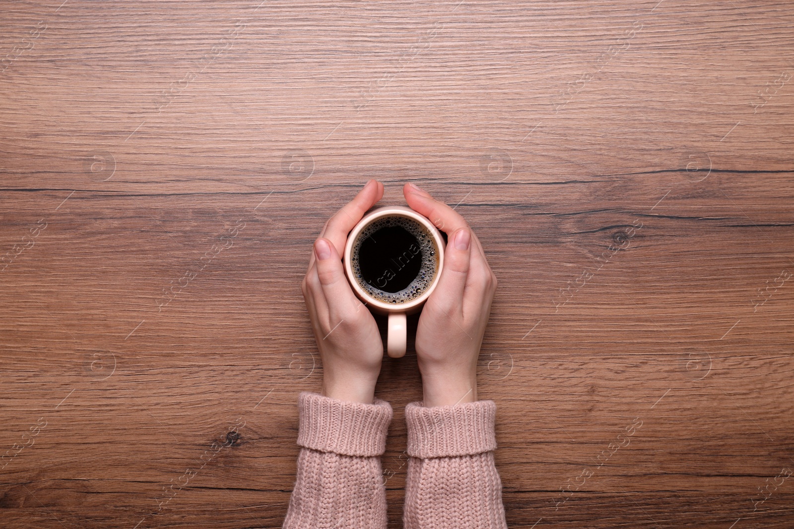 Photo of Woman with cup of coffee at wooden table, top view