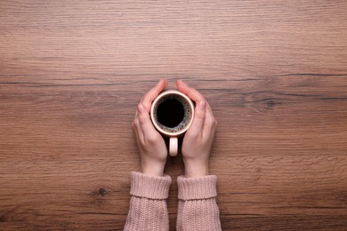 Photo of Woman with cup of coffee at wooden table, top view