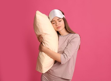 Photo of Young woman wearing pajamas and mask with pillow in sleepwalking state on pink background