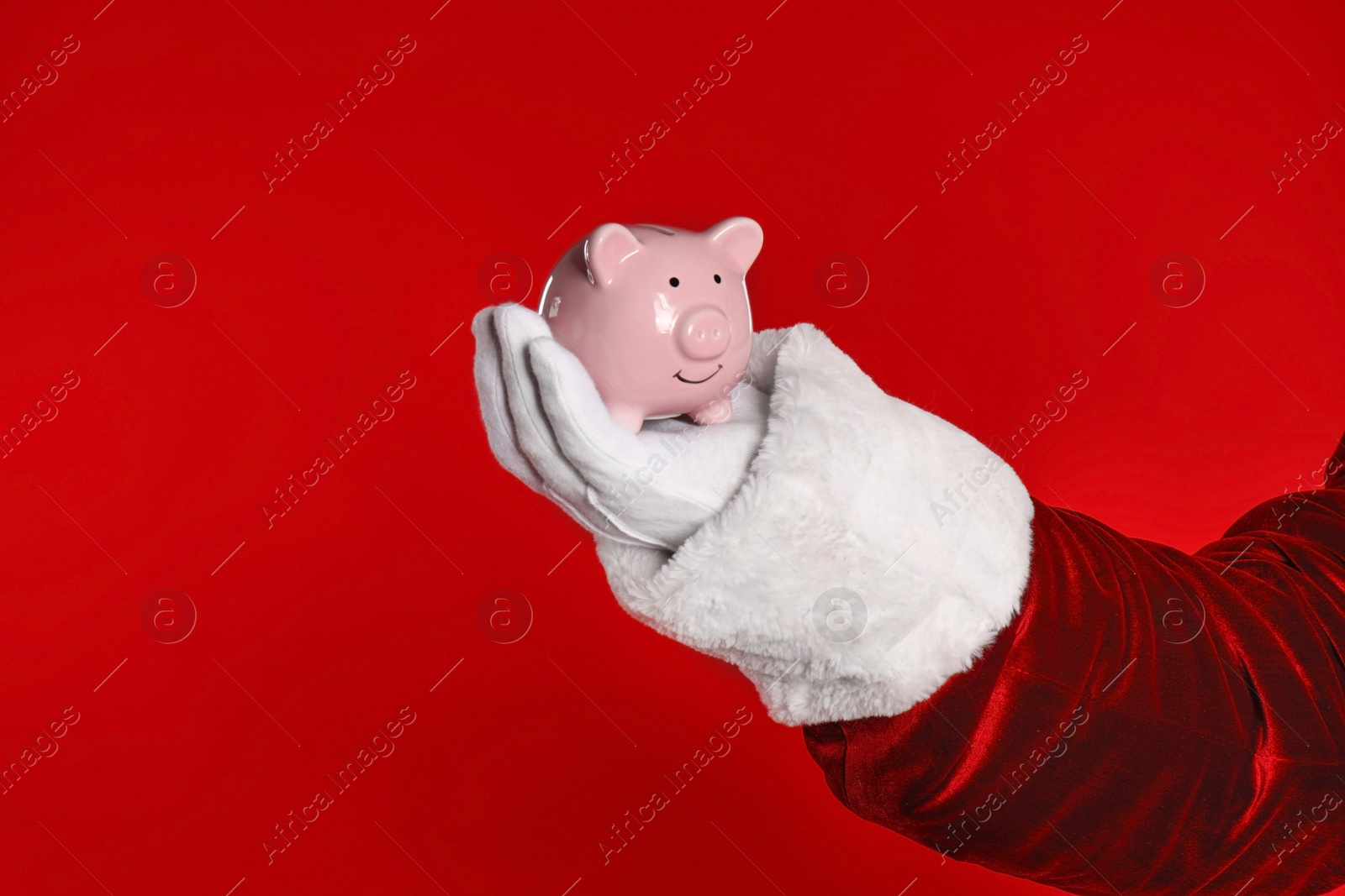 Photo of Santa Claus holding piggy bank on red background, closeup