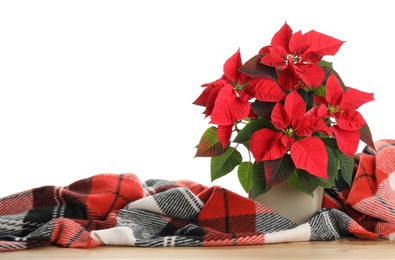 Red Poinsettia in pot and warm plaid on wooden table, space for text. Christmas traditional flower