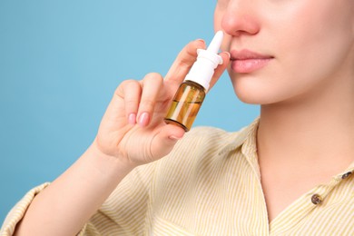 Woman using nasal spray on light blue background, closeup