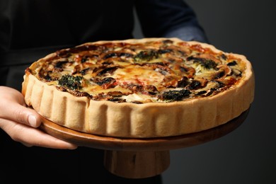 Photo of Woman holding delicious quiche with mushrooms on dark grey background, closeup