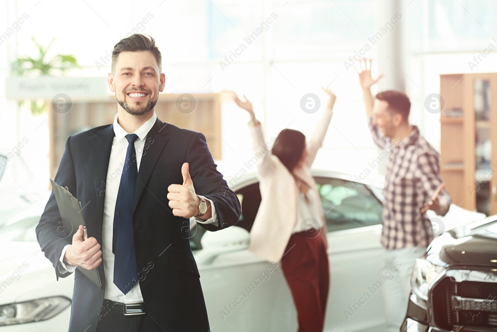 Photo of Salesman with clipboard and happy couple in salon. Buying new car