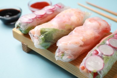 Different delicious spring rolls wrapped in rice paper on light blue background, closeup