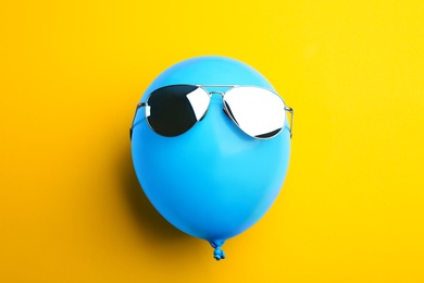 Balloon with stylish sunglasses on yellow background, top view