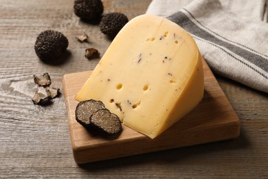 Photo of Delicious cheese and fresh black truffles on wooden table