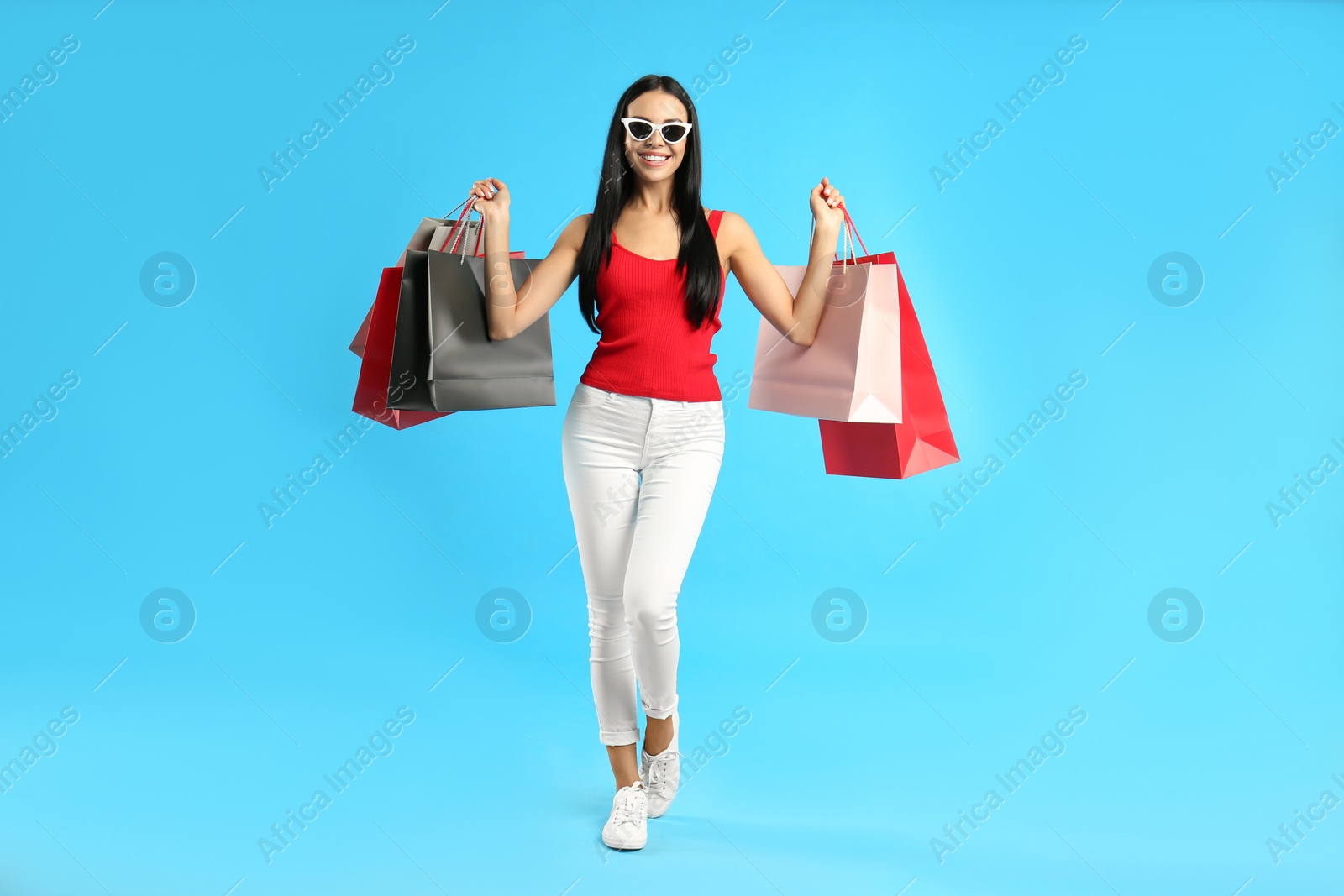 Photo of Beautiful young woman with paper shopping bags on light blue background