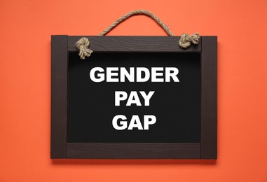 Photo of Blackboard with words Gender Pay Gap on orange background, top view