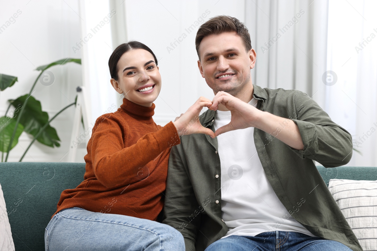 Photo of Happy couple making heart with hands at home