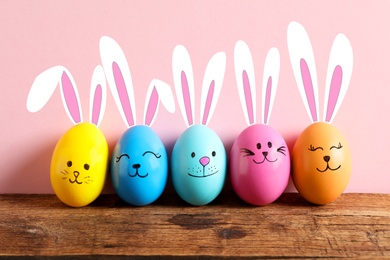 Image of Colorful eggs as Easter bunnies on wooden table against pink background