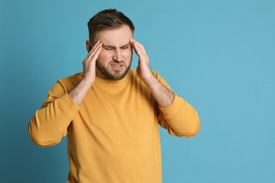Photo of Man suffering from migraine on light blue background, space for text