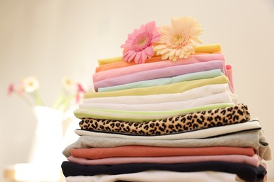 Stack of clean clothes and flowers on blurred background, closeup