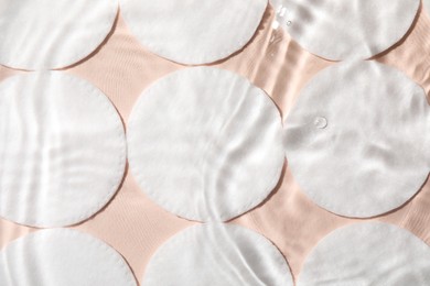 Photo of Many cotton pads in water on beige background, flat lay