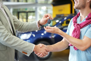 Salesman shaking hands with customer while giving car key in auto dealership, closeup