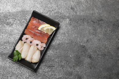 Sashimi set served with lemon and parsley on light grey table, top view. Space for text