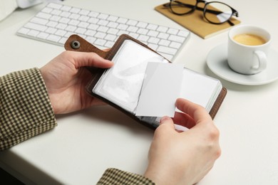 Woman holding leather business card holder with blank cards at white table, closeup