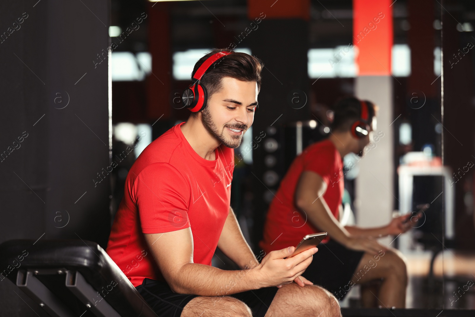 Photo of Young man with headphones listening to music on mobile device at gym