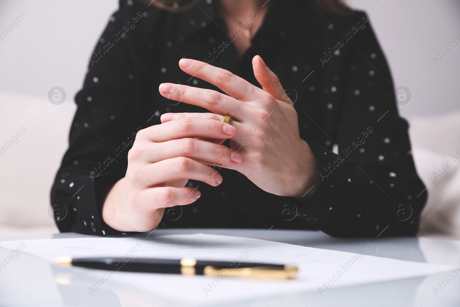 Photo of Woman taking off wedding ring at table indoors, closeup. Divorce concept