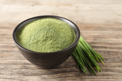 Photo of Wheat grass powder in bowl and fresh sprouts on wooden table, closeup