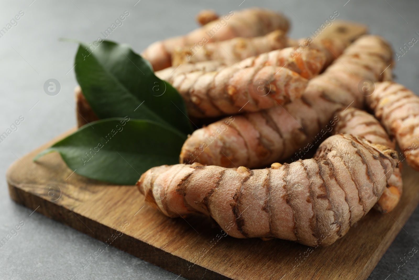 Photo of Many raw turmeric roots and green leaves on grey table, closeup