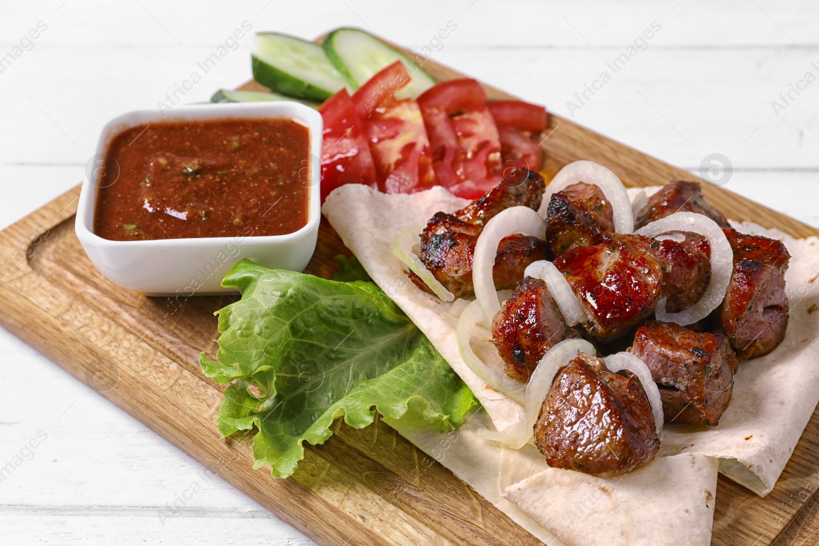 Photo of Wooden board with juicy shish kebab and sauce, closeup