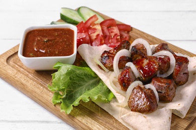 Wooden board with juicy shish kebab and sauce, closeup