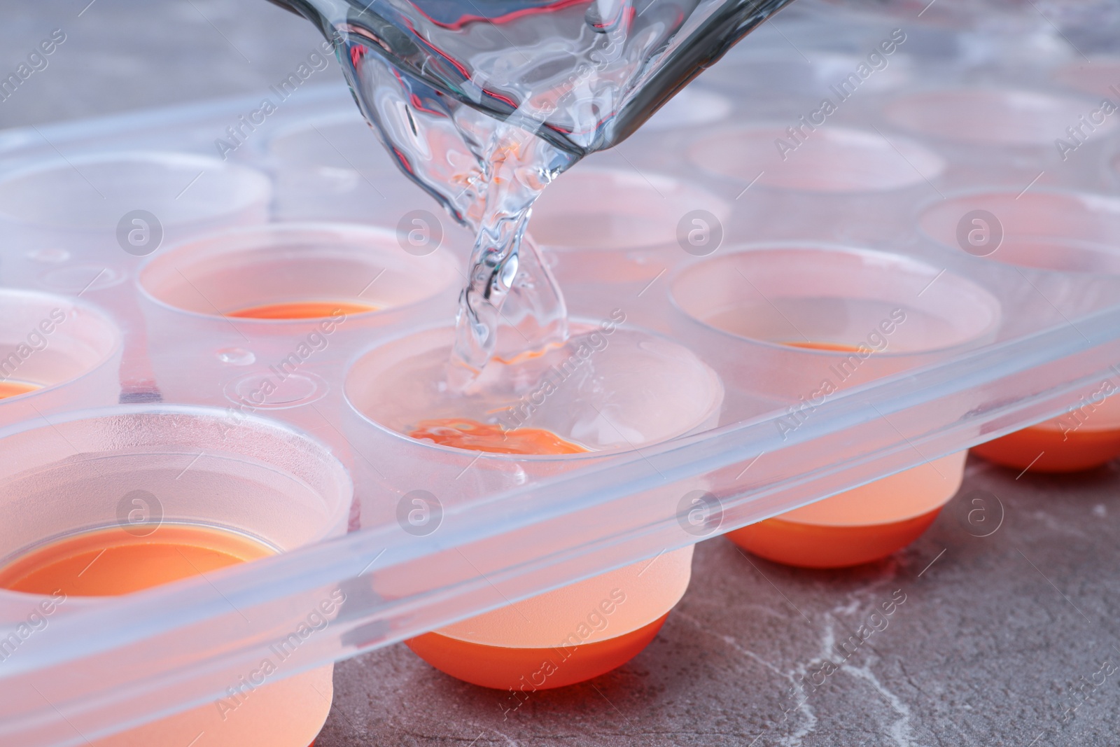 Photo of Pouring water into ice cube tray on grey marble table, closeup