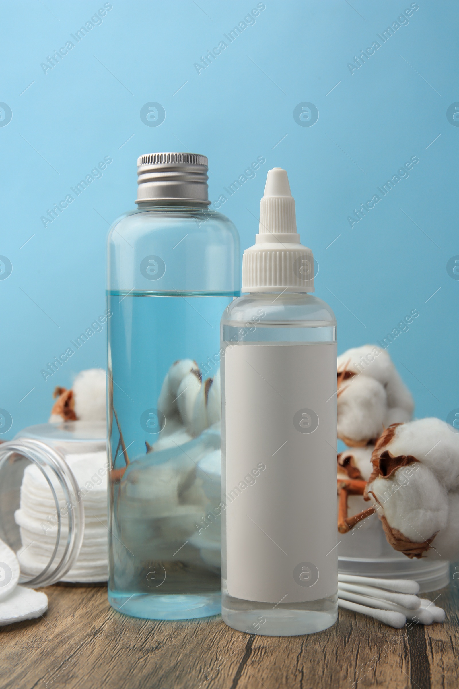 Photo of Composition with makeup removers and cotton flowers on wooden table against light blue background