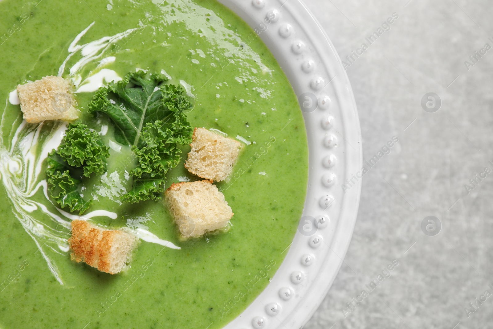 Photo of Tasty kale soup with croutons on grey table, top view