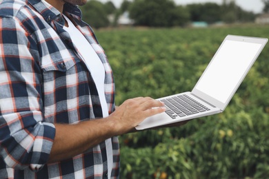 Photo of Man using laptop with blank screen in field, closeup. Agriculture technology