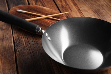 Photo of Empty iron wok and chopsticks on wooden table, closeup