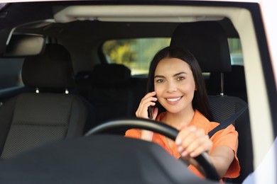 Photo of Happy young woman talking on smartphone in modern car, view through windshield