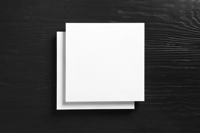 Stack of blank paper sheets for brochure on black wooden background, top view. Mock up