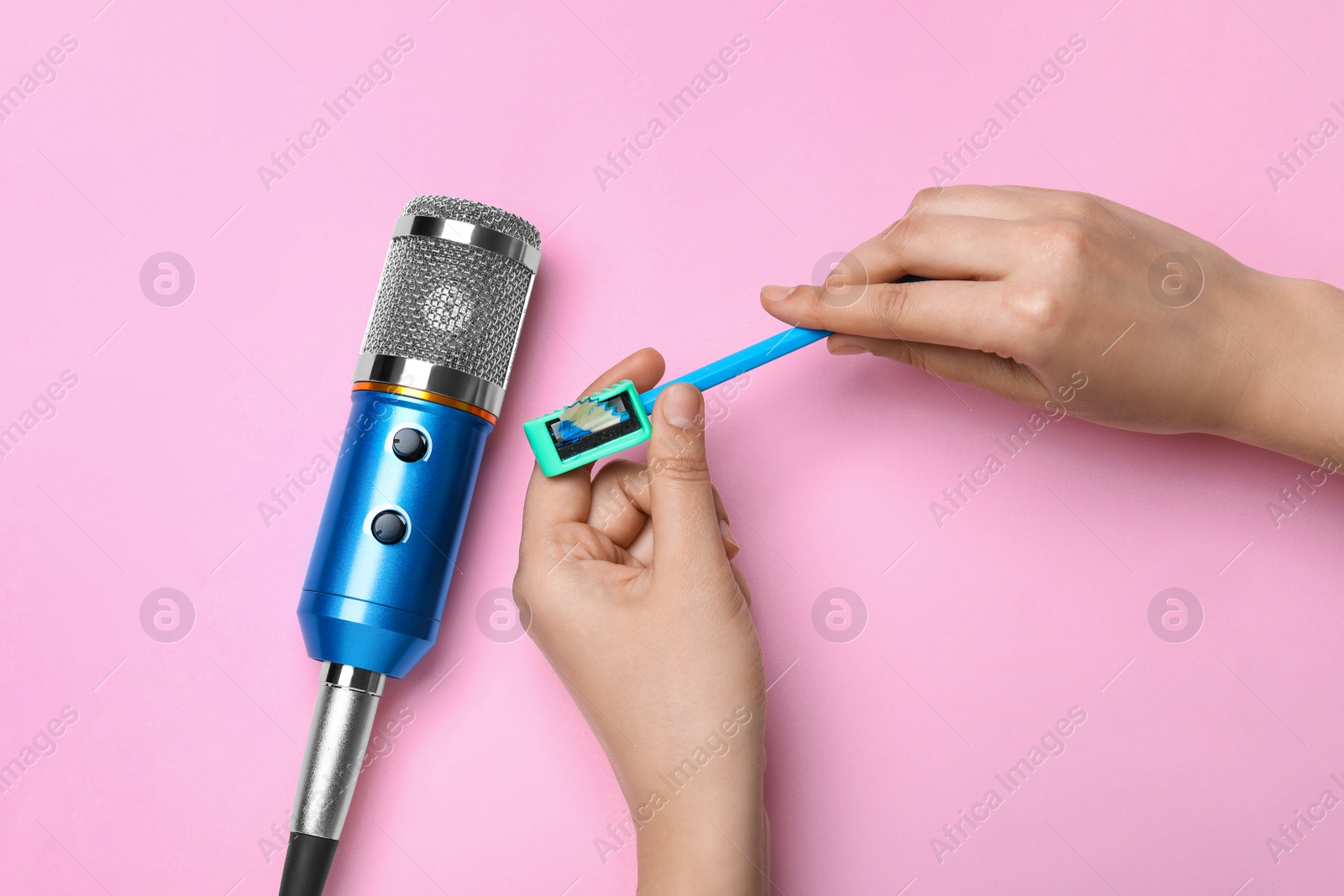 Photo of Woman making ASMR sounds with microphone, pencil and sharpener on pink background, top view