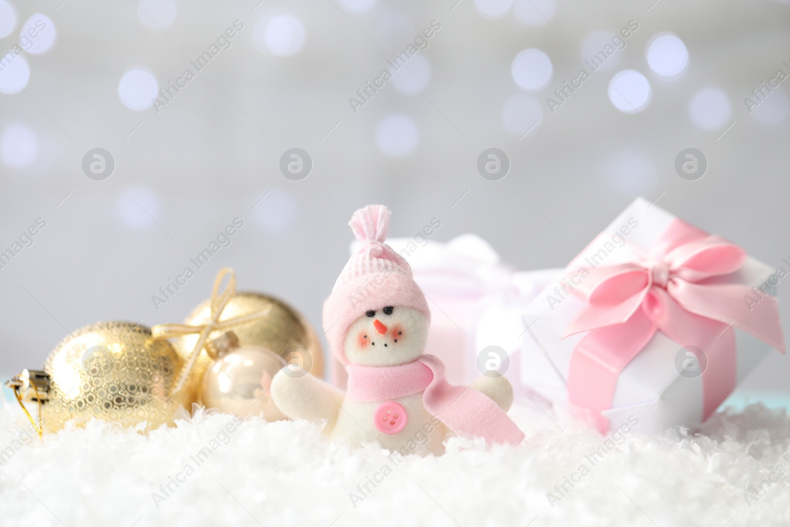 Photo of Snowman toy, gift box and Christmas balls on snow against blurred festive lights