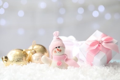 Photo of Snowman toy, gift box and Christmas balls on snow against blurred festive lights